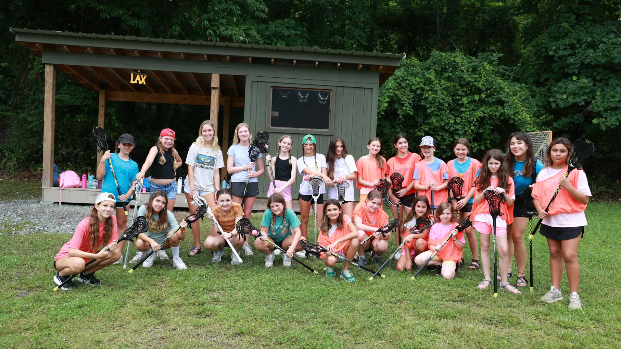 Group of Camp Highlander girl campers holding lacrosse sticks outside the camp LAX shed in Mills River, North Carolina